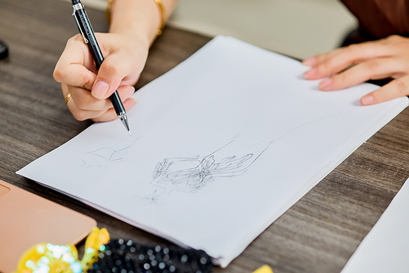 Boceto de alta costura dibujado a mano en un escritorio junto a materiales de pedrería