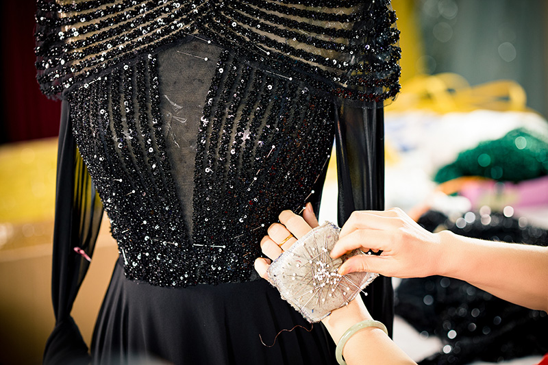 Trabajadora sujetando y fijando adornos de lentejuelas en un cuerpo de vestido negro
